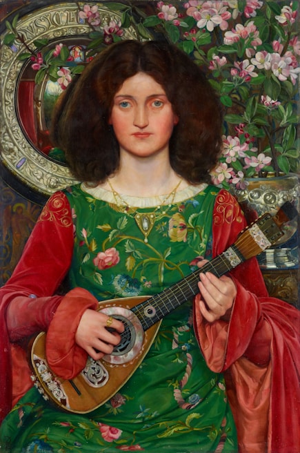 A woman with long, curly brown hair is dressed in an ornate, green floral gown with red sleeves. She holds a string instrument resembling a mandolin or lute. In the background, there is an intricate floral pattern and decorative items including a round mirror with decorative elements and a large vase of pink flowers.