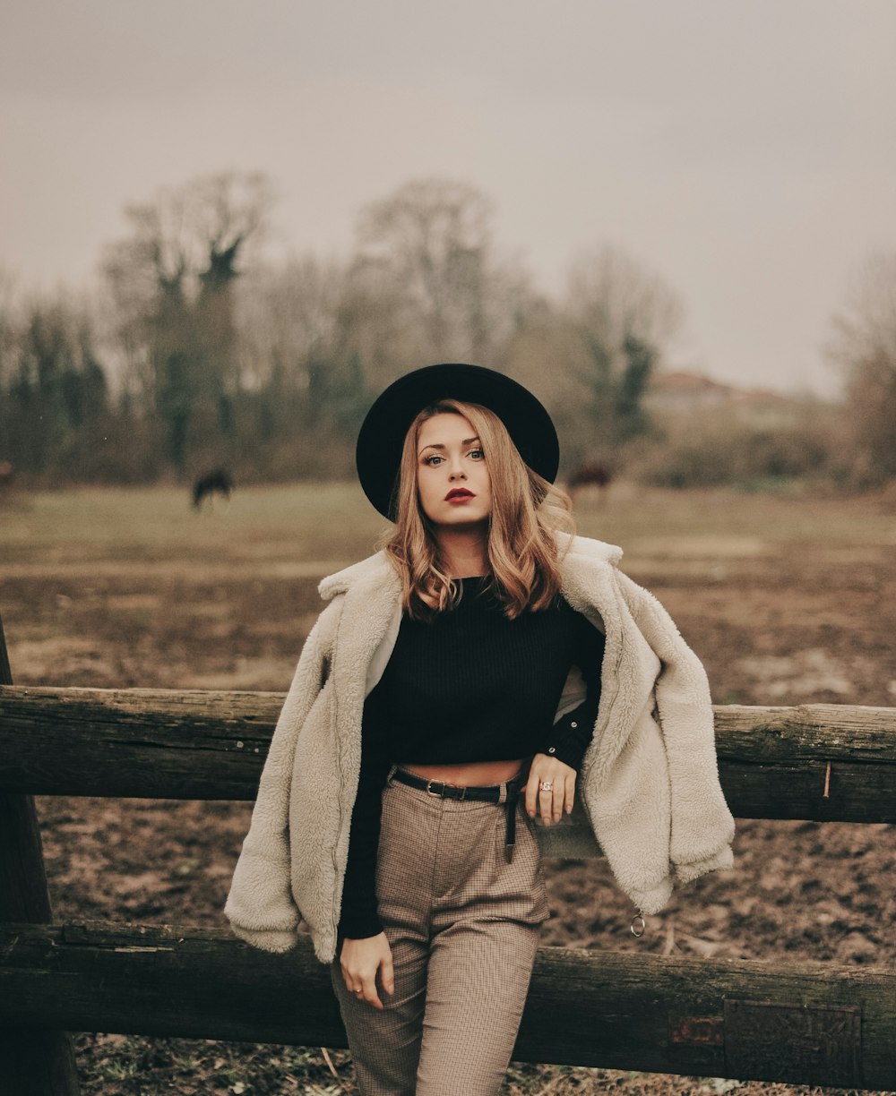 woman in black crop top and brown pants leaning on log fence