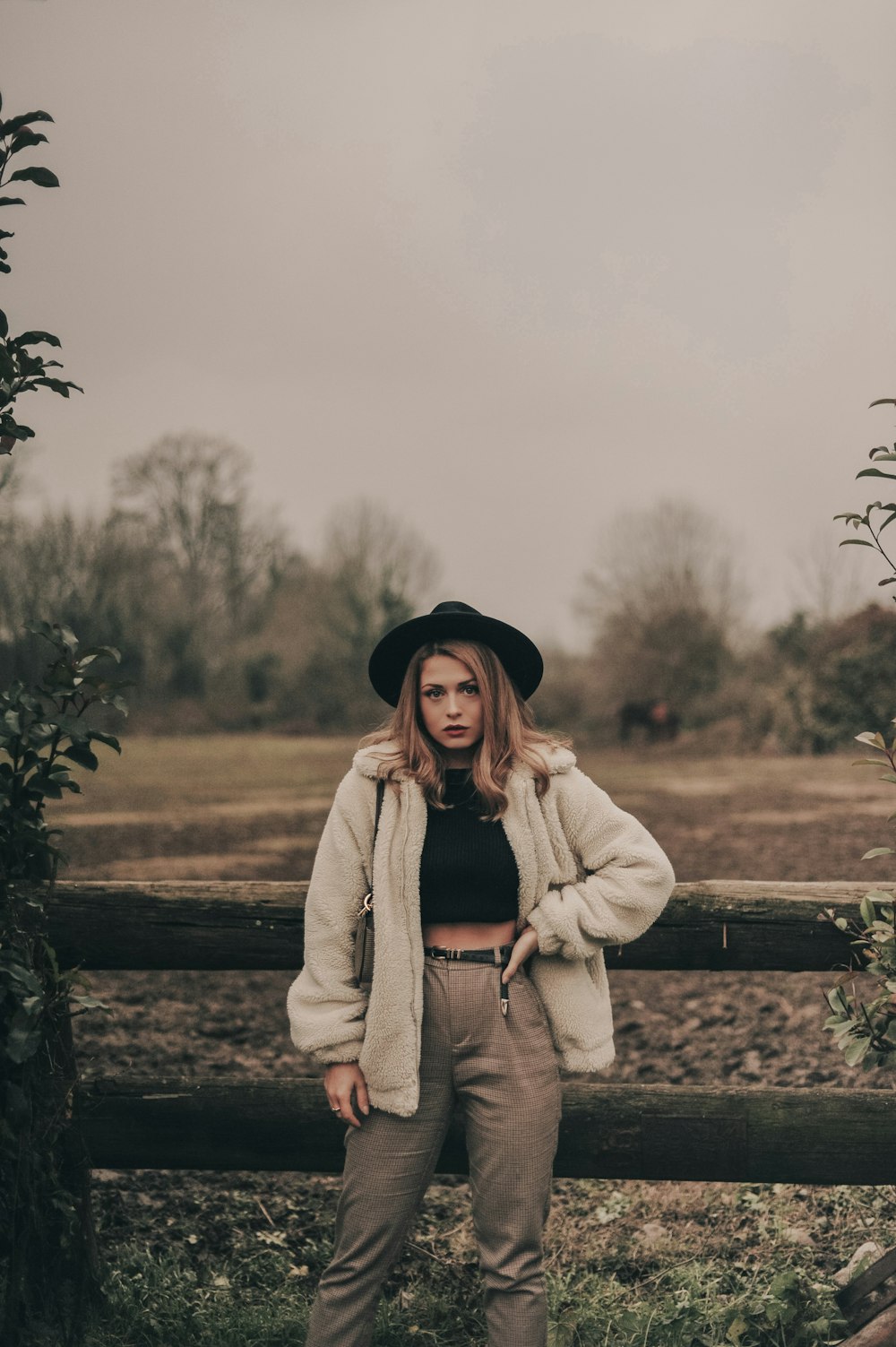 woman in coat and hat standing beside fence