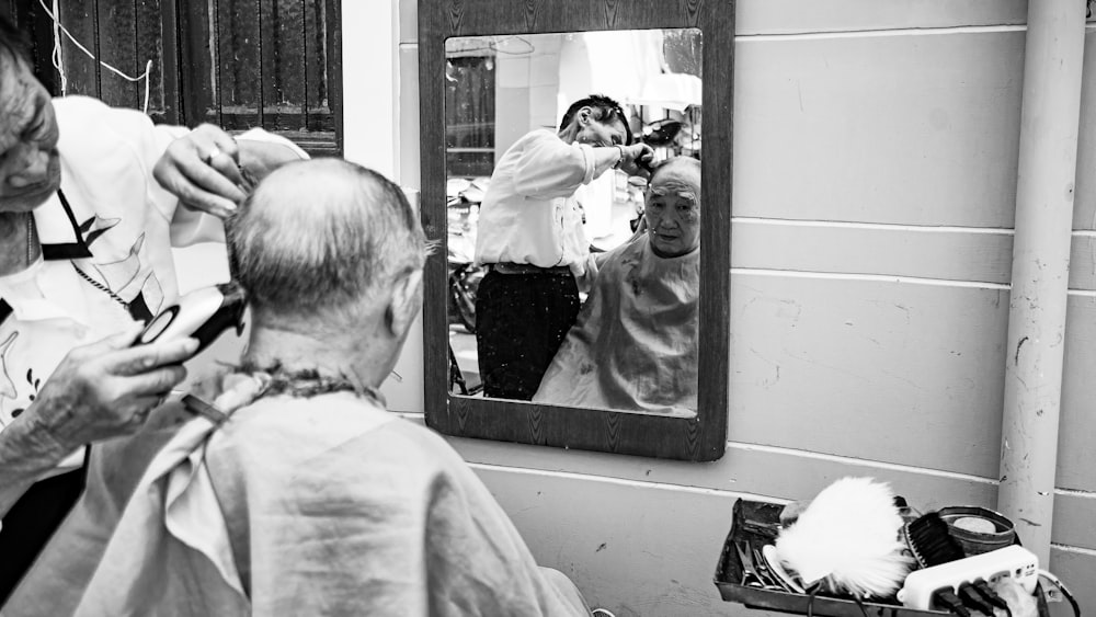 grayscale photo of man doing haircut