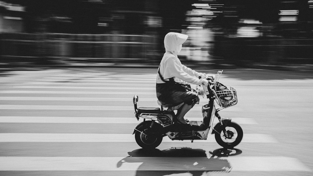 grayscale photo of person riding motor scooter