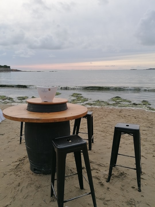 round black and brown table beside three black stools on shore during day in Mesquer France