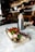 A charcuterie board on a marble table holding a variety of meats, cheeses, olives, and grapes, accompanied by a glass of champagne with a strawberry garnish and a bottle in an ice bucket. The background is a blurred view of a bar with dim lighting.