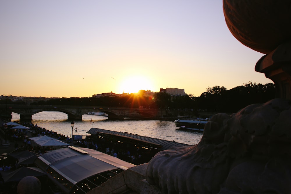 the sun is setting over a river with a bridge in the background