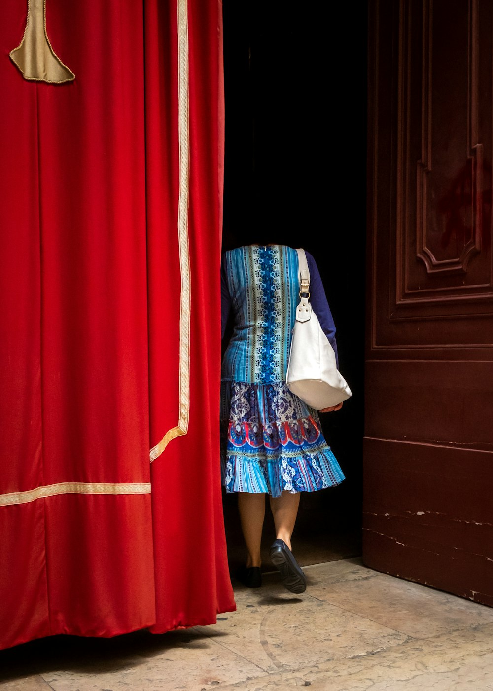 woman wearing blue and multicolored dress with white shoulder bag walking and going inside building