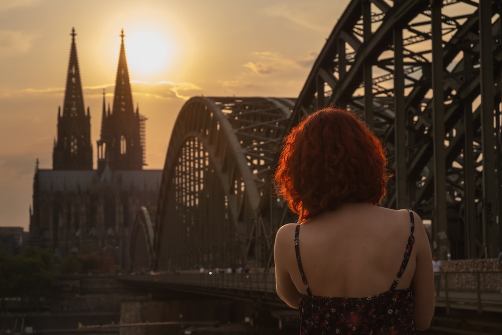 woman wearing black and multicolored spaghetti strap top standing while facing back near Cologne Cathedral in Germany