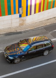 A vibrant car wrapped in a bold, colorful design parked outside a creative studio.