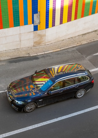 A vibrant car wrapped in a bold, colorful design parked outside a creative studio.