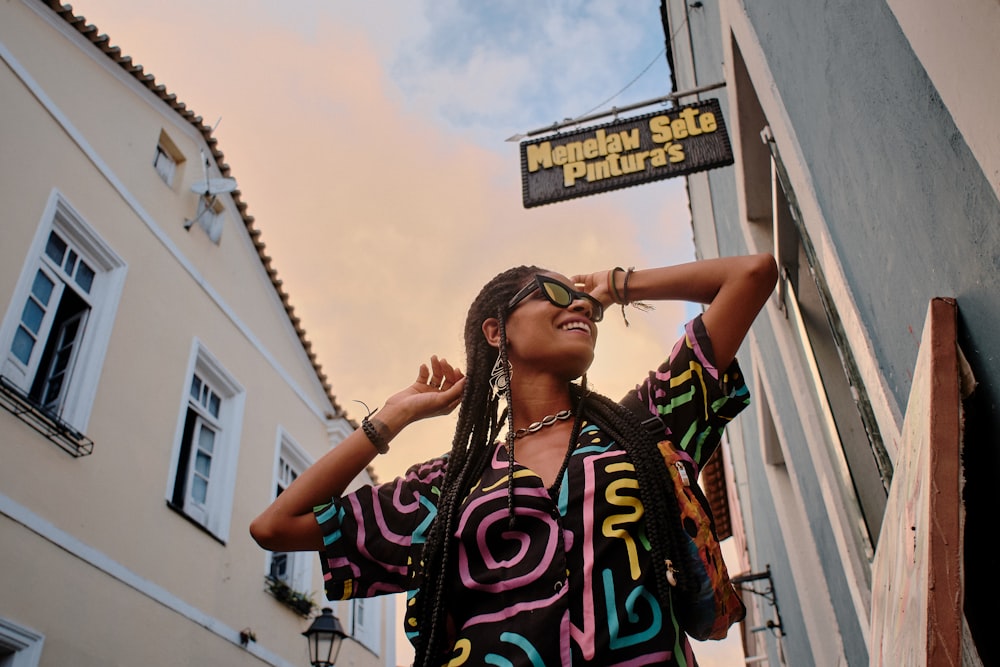 smiling woman wearing black and pink blouse and black sunglasses standing beside building