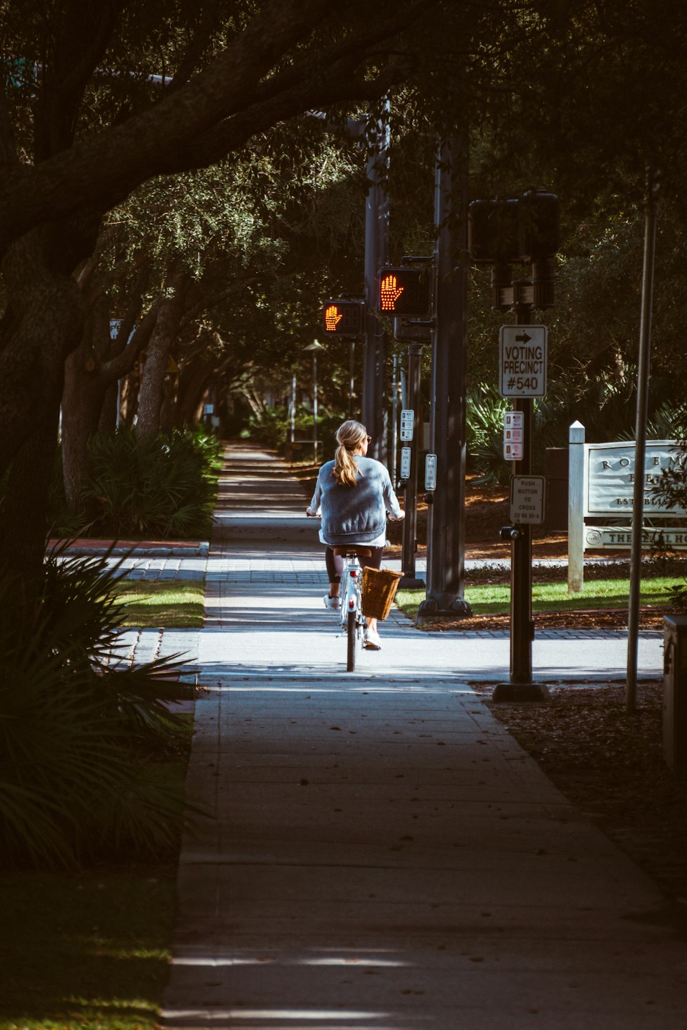 woman riding bike on sidewalk near trees and traffic lights