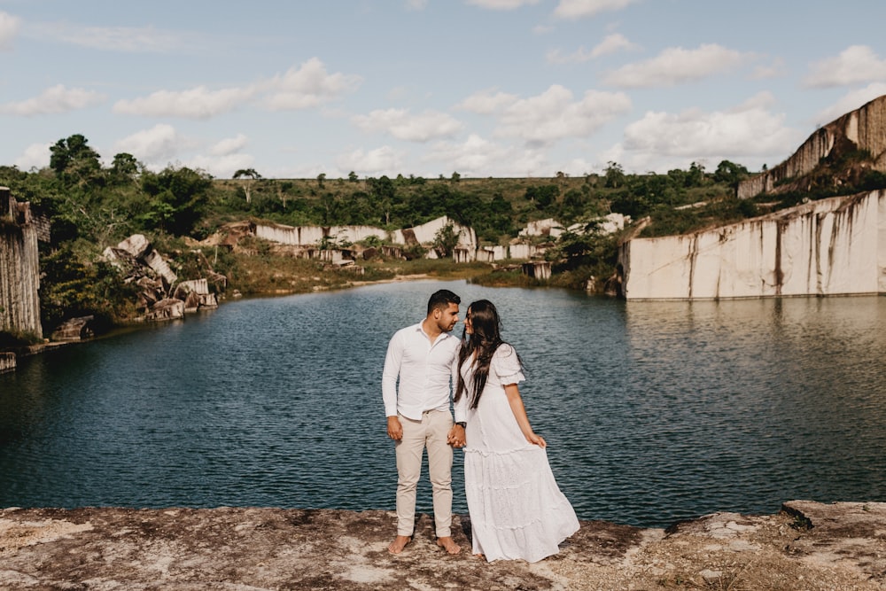 man and woman standing on cliff near body of water