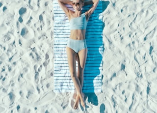 woman lying on sand with towel during daytime