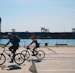 two people cycling near body of water during daytime