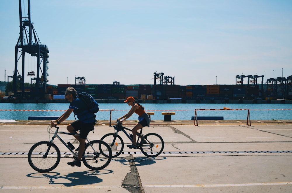 two people cycling near body of water during daytime