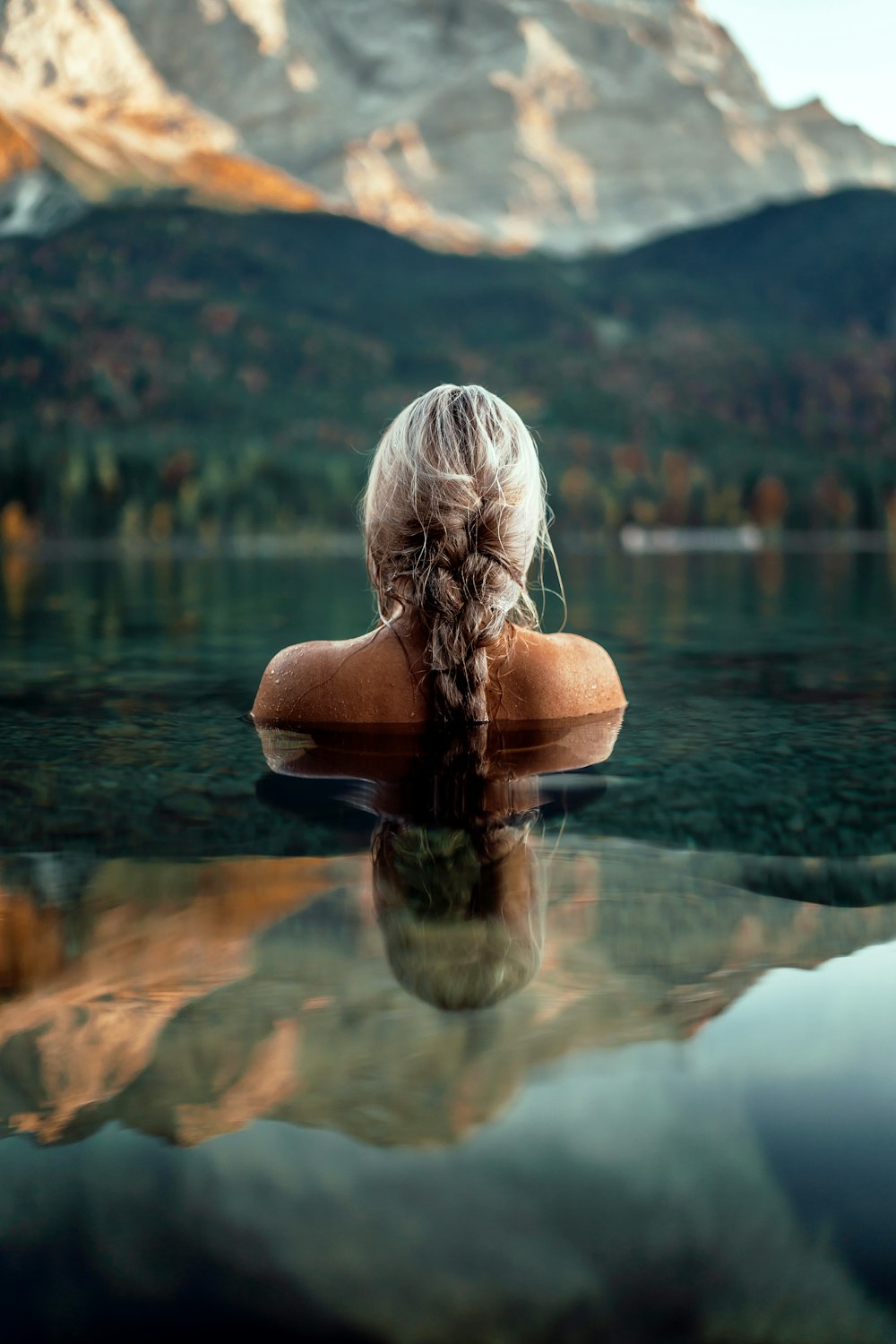 femme à moitié immergée dans l’eau face à la montagne pendant la journée