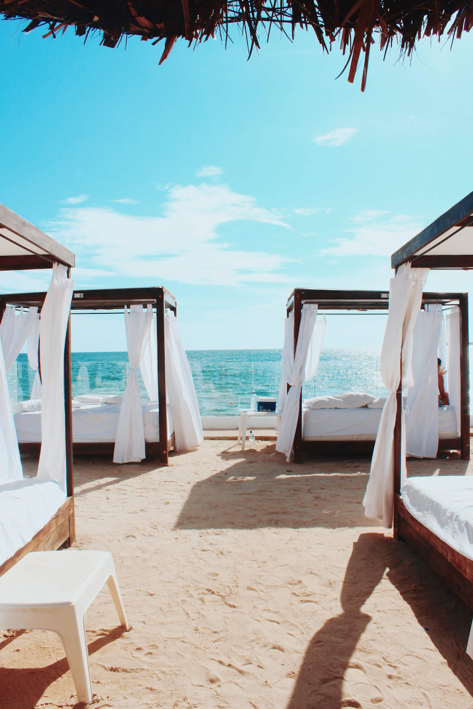 Three large canopy-style beds on sandy shore with white curtains facing the ocean