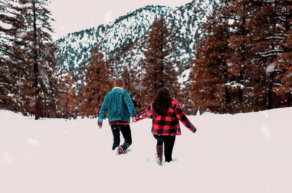 shallow focus photo of man and woman holding each others hands on snowfield during daytime