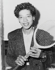 A candid photo of Ava Tang smiling while holding a tennis racket on a sunny day.