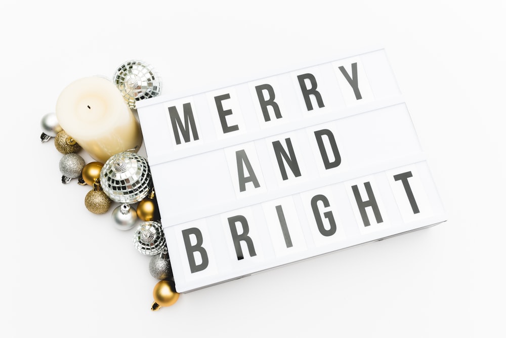 silver and gold baubles beside candle and signage with Merry and Bright print