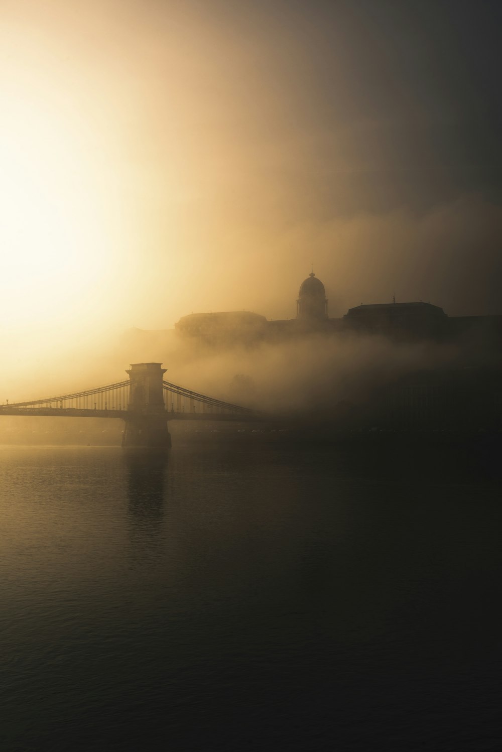 a foggy sunrise over a bridge and a body of water