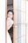 A bride stands partially behind a sliding wooden door with frosted glass panels. She is smiling warmly, with her hand touching her face, showcasing delicate earrings and a lace wedding dress. The setting appears serene and bright, with soft light illuminating her features.
