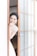 A bride stands partially behind a sliding wooden door with frosted glass panels. She is smiling warmly, with her hand touching her face, showcasing delicate earrings and a lace wedding dress. The setting appears serene and bright, with soft light illuminating her features.