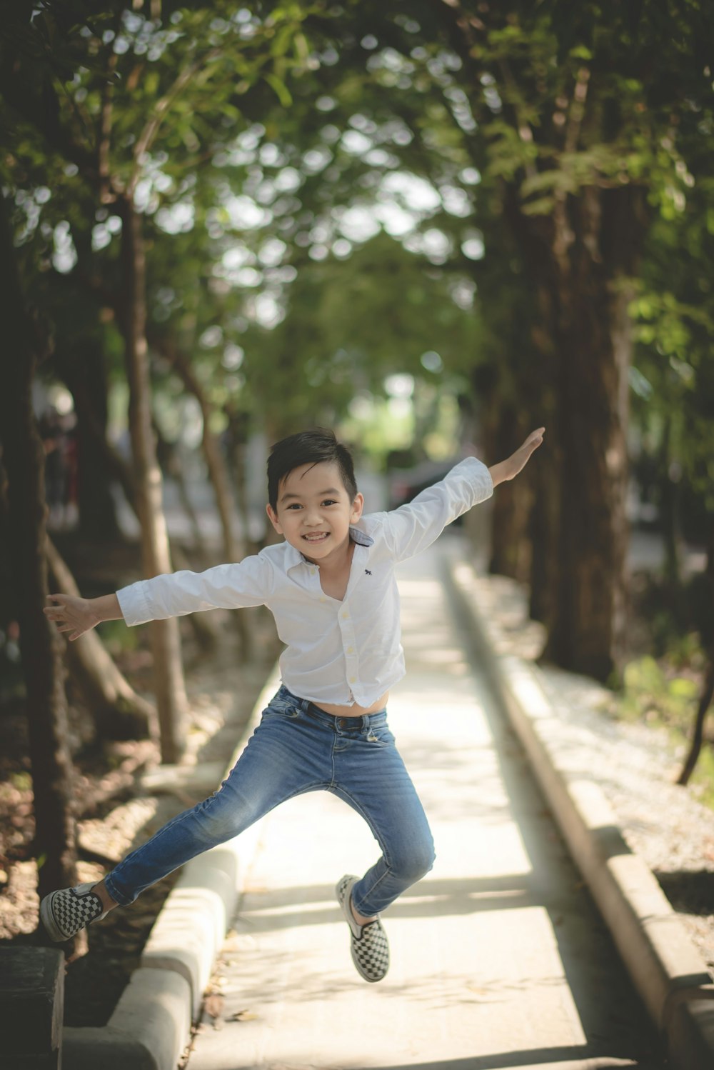 boy in white long-sleeved shirt and blue denim jeans jumping on sidewalk