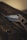 A folding knife partially open, resting on a dark wooden surface. The knife handle appears textured and the blade is engraved with the brand 'Smith & Wesson Extreme Ops'. The lighting is dim and atmospheric.