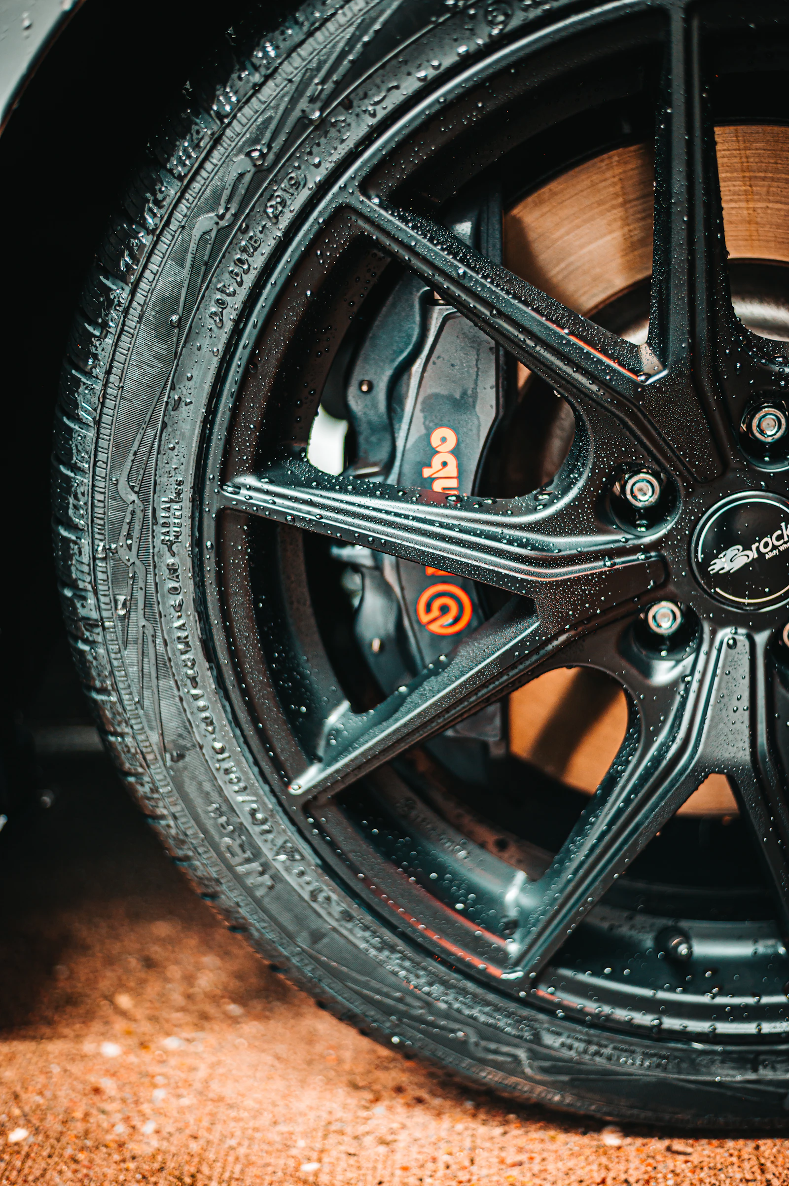 Close-up of a gloss black multi-spoke alloy wheel, beaded with water after refinishing.
