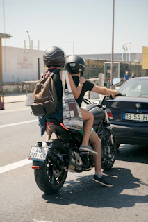 A friendly motoveloce rider helping a passenger put on a helmet before a city ride at sunset.