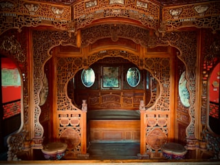 Intricately carved wooden interior featuring ornate designs and elaborate patterns. The space includes circular windows and traditional motifs, creating a symmetrical and visually striking environment.