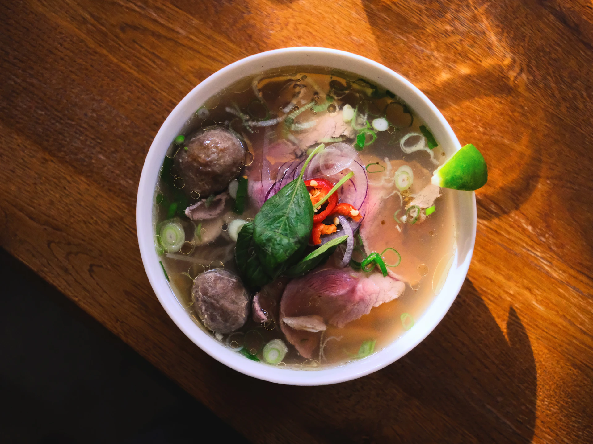 A top-down bowl of phở with rare beef, lime and fresh herbs