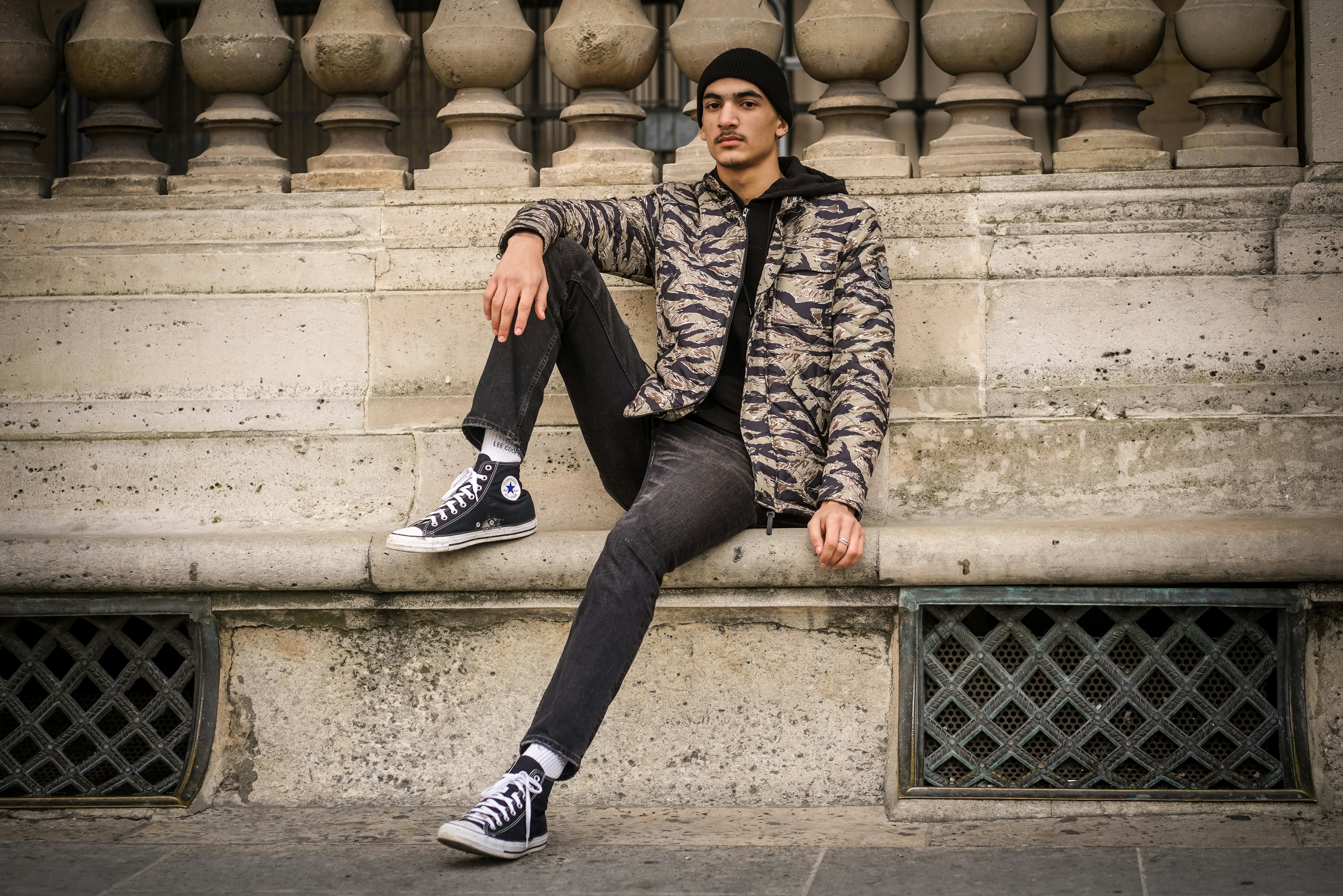 man wearing gray and black jacket sitting beside wall