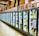 A row of brightly lit commercial refrigerators filled with various packaged foods, predominantly frozen goods. The tops of the refrigerators display a variety of cardboard boxes and posters featuring different products and individuals. The scene is set in a spacious supermarket or grocery store aisle with a reflective tile floor.