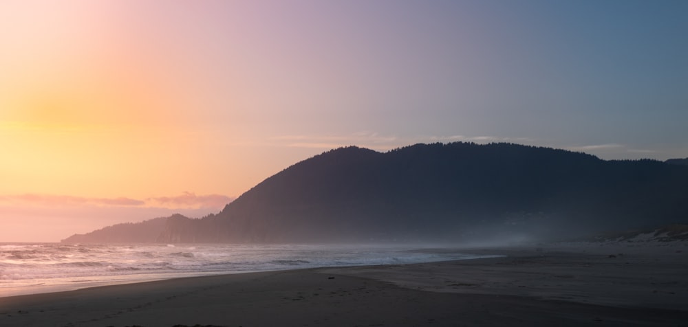 the sun is setting on a beach with mountains in the background