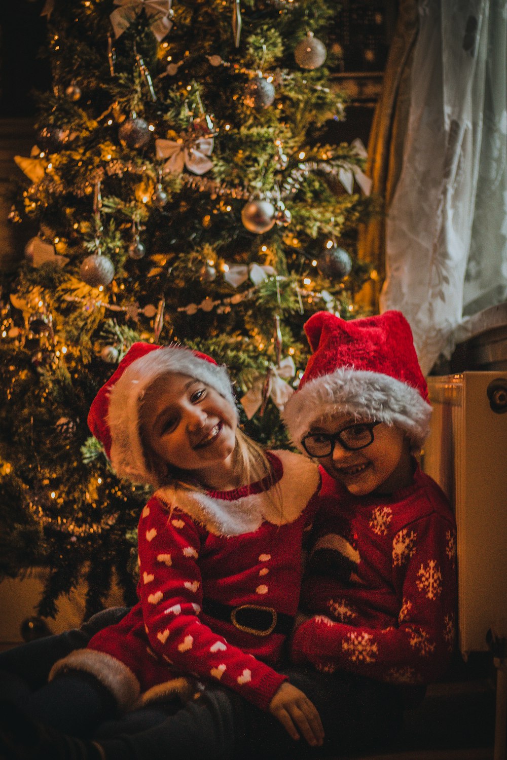 two toddlers in red suits beside Christmas tree