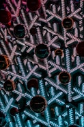 Intricate snowflake-shaped structures lit with bright white and blue LED lights create a mesmerizing pattern. Large, shiny red ornaments are interspersed, adding contrast and depth to the arrangement.