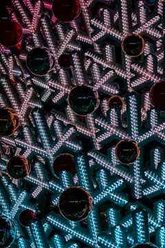 Intricate snowflake-shaped structures lit with bright white and blue LED lights create a mesmerizing pattern. Large, shiny red ornaments are interspersed, adding contrast and depth to the arrangement.