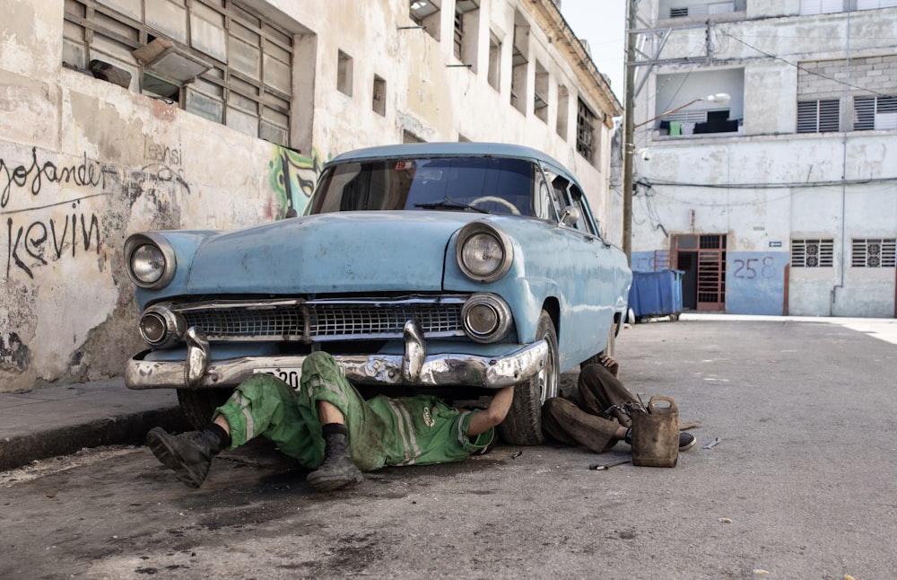 a man laying on the ground next to a blue car