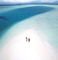 A couple walking hand-in-hand along a pristine white sand beach with crystal-clear waves gently lapping at their feet.