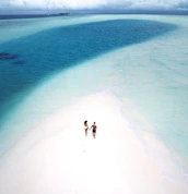 Close-up of a couple holding hands, walking along a pristine white sand beach at dusk.
