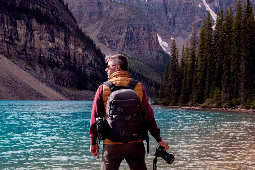 standing man carrying black backpack in front of body of water