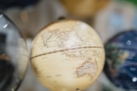 A close-up of a globe features detailed geographical markings, prominently displaying parts of Southeast Asia and the Indian Ocean. The globe's surface has a muted, vintage tone, and the background is softly blurred, highlighting the globe.