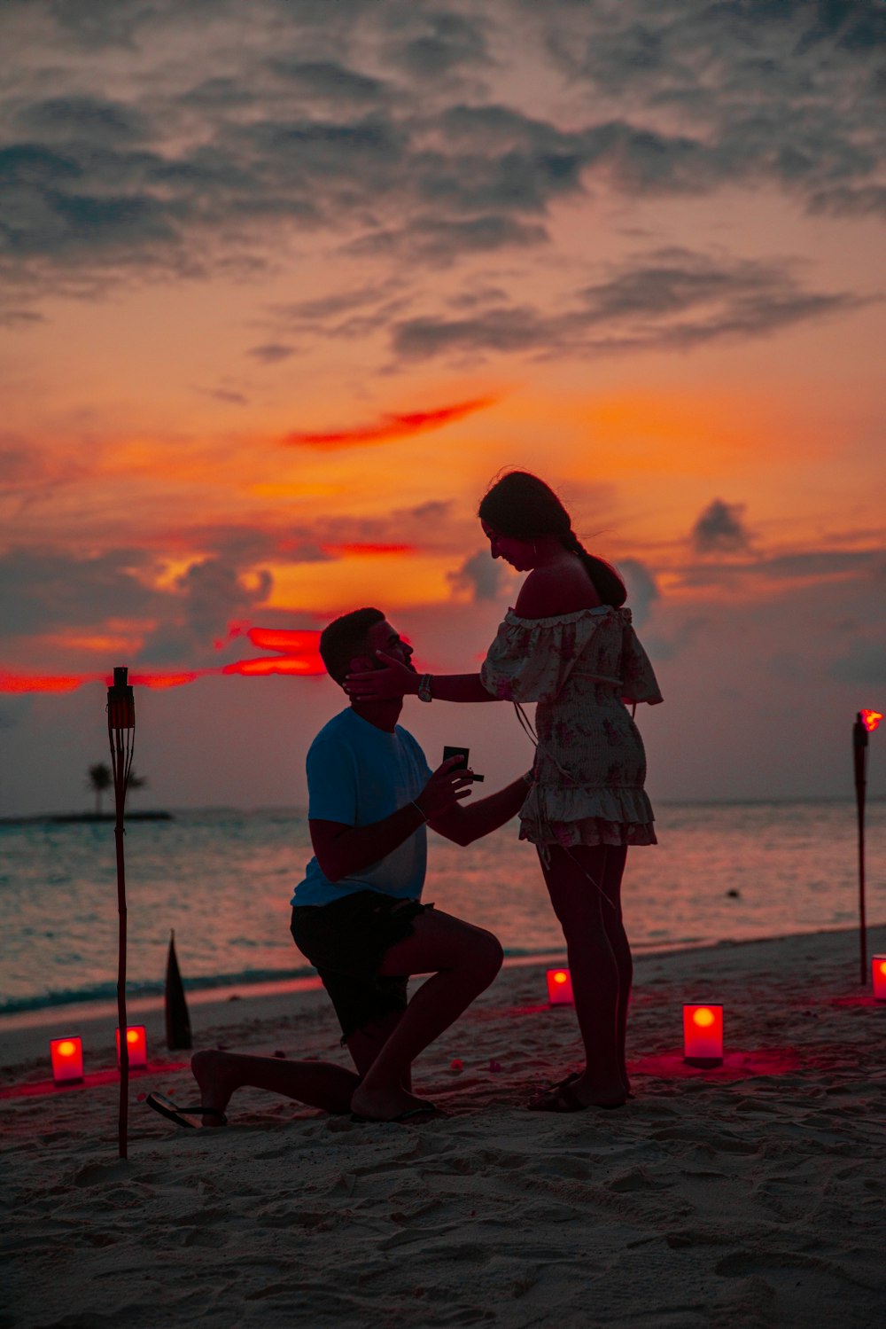 homme agenouillé devant une femme au bord de la plage pendant l’heure dorée