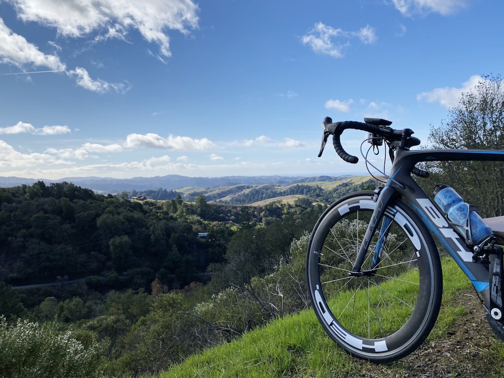 gray and blue road bike on cliff viewing mountain under white and blue sky