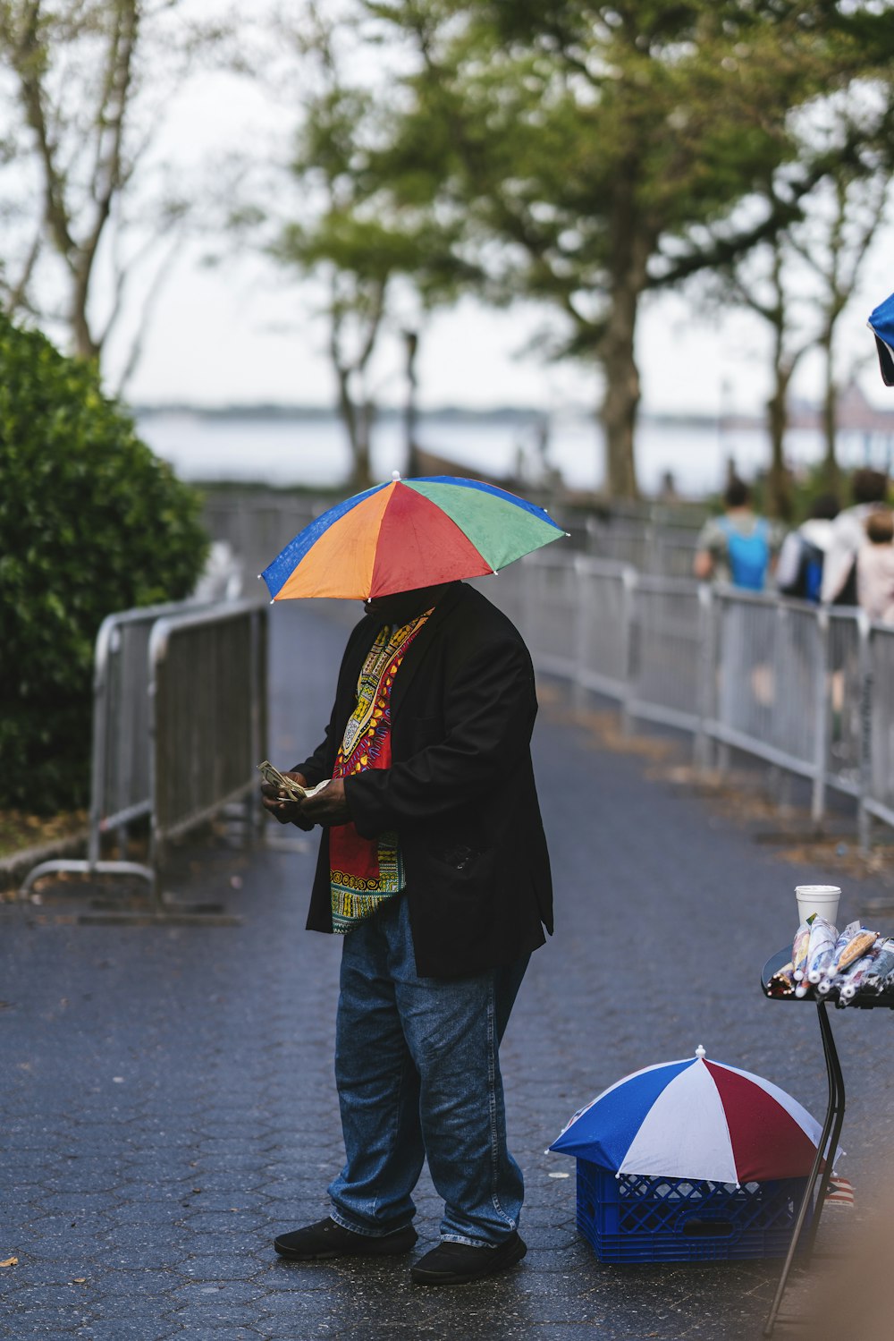 色とりどりの傘をさした男が歩道に立っていて、昼間は他の人が歩いている