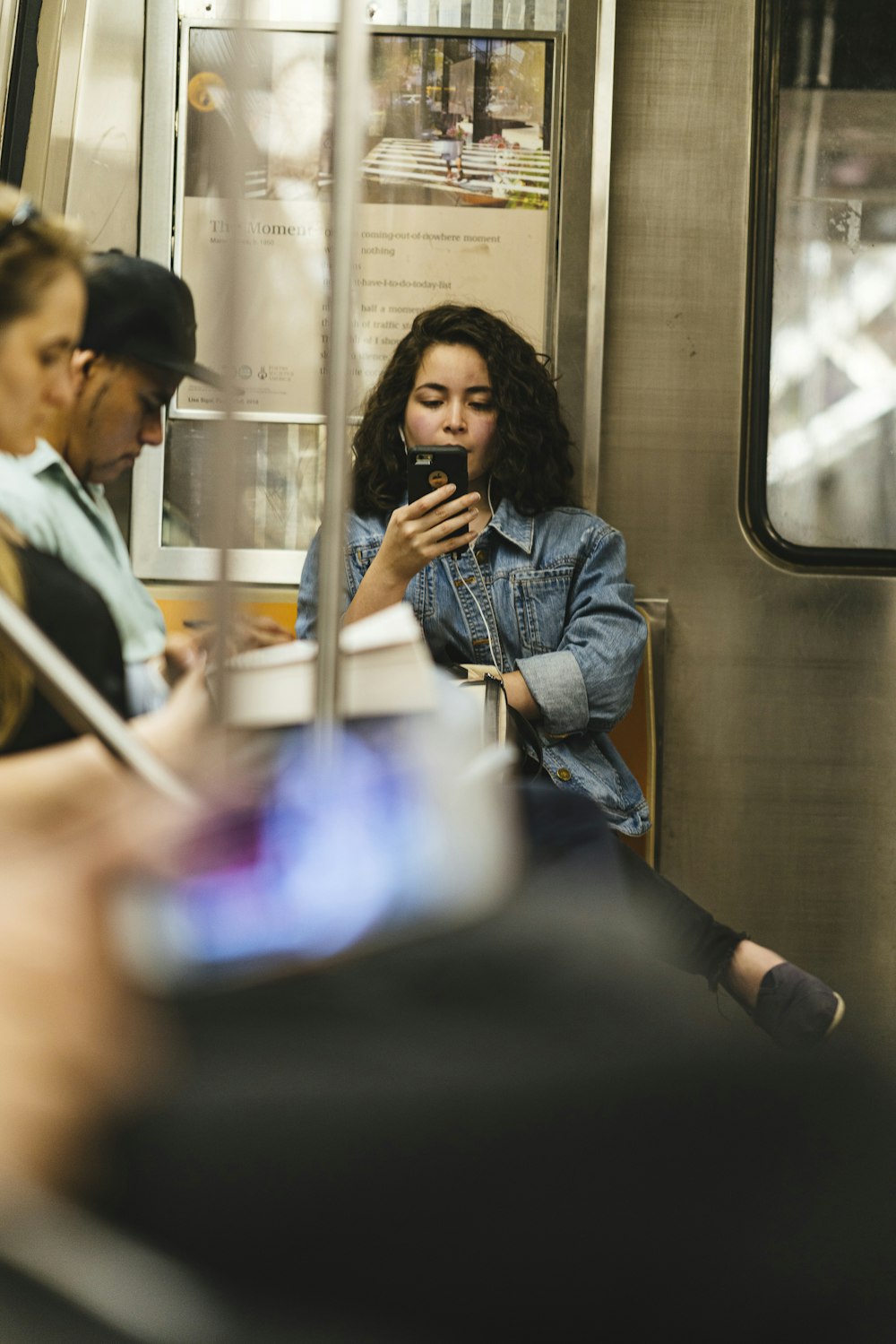 woman wearing blue denim jacket using phone while sitting near other people
