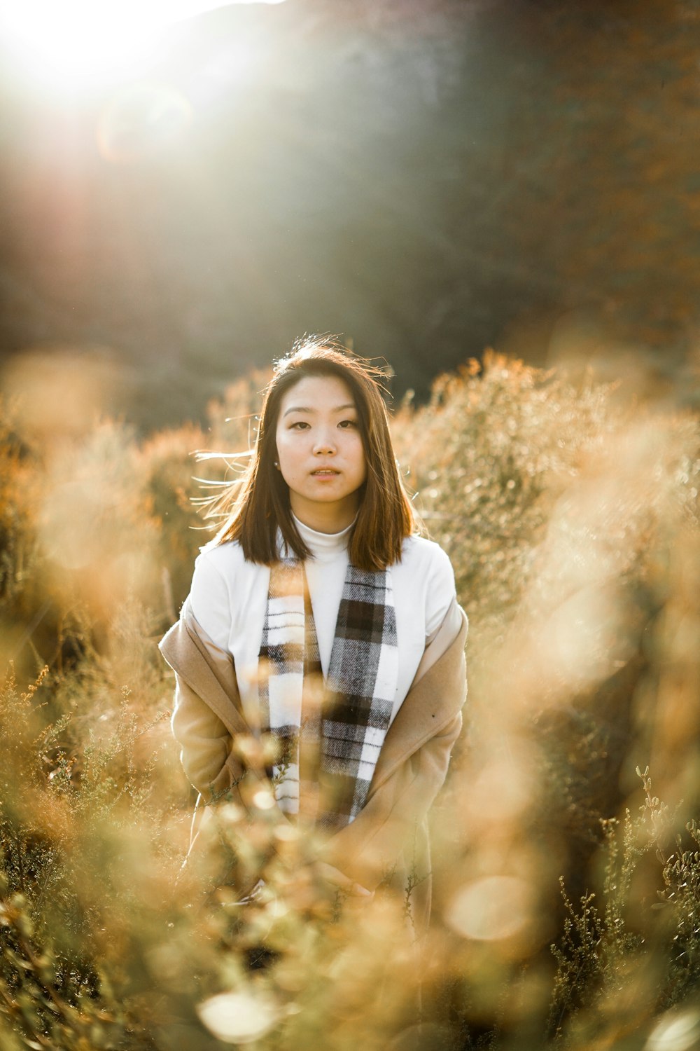 woman wearing brown jacket standing near plants during daytime