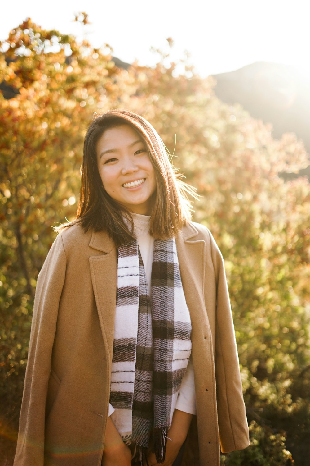 smiling woman wearing brown coat standing near green plant