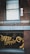 A vintage-style barbershop with brick walls and a large window displaying ornate gold lettering spelling 'Derby Supply Co'. A classic barber pole is mounted on the building's exterior. Inside, a barber is attending to a customer in a chair.